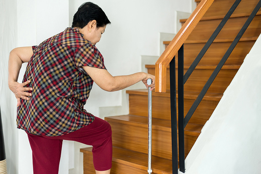 older woman suffering from low-back lumbar pain while walking on stair at home